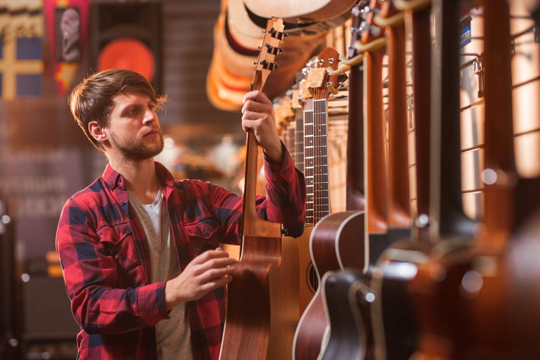 a-young-man-choosing-a-guitar-in-a-store Young man choosing a guitar in a music store.